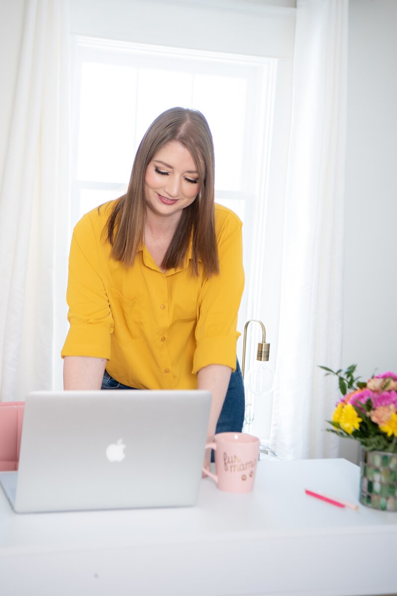 Tara Reid in a yellow blouse typing on a laptop at her desk