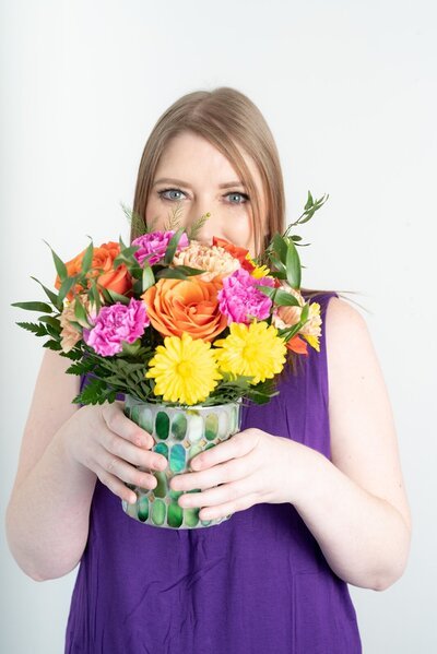 Tara Reid smiling behind a bright bouquet of flowers