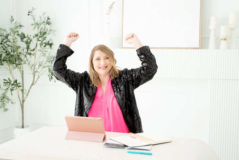Tara Reid at her desk with both arms raised in celebration